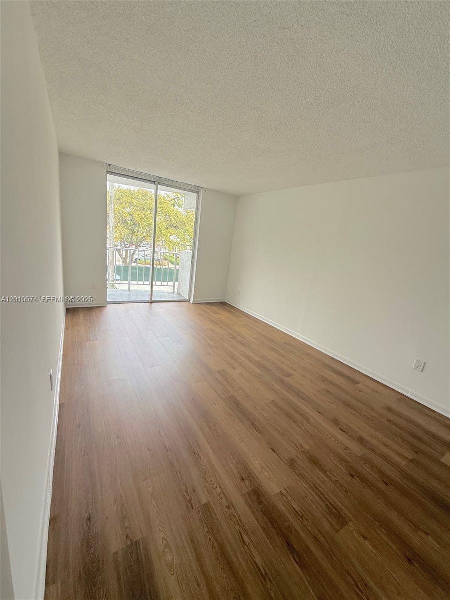 An empty room features light wood-look flooring, white walls, and a sliding glass balcony door — 482 NW 165th St Rd # 307, Miami FL 33169, MIAMI, FL