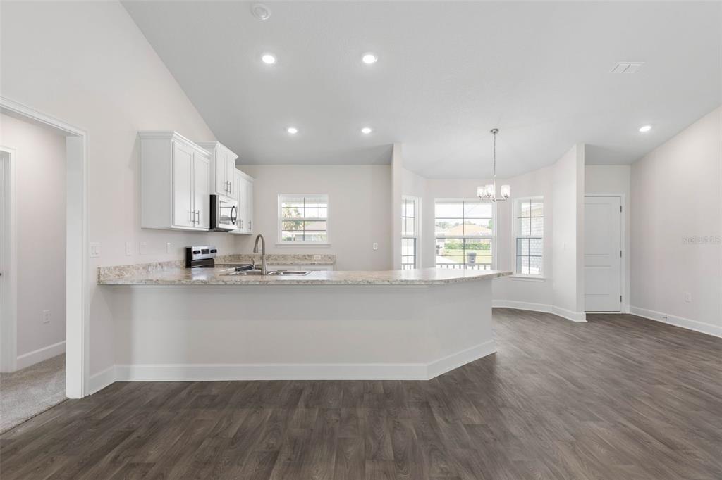 A kitchen with white cabinets, granite countertops, and a breakfast bar overlooking a dining area — 2 ULMACEAL PATH, PALM COAST, FL
