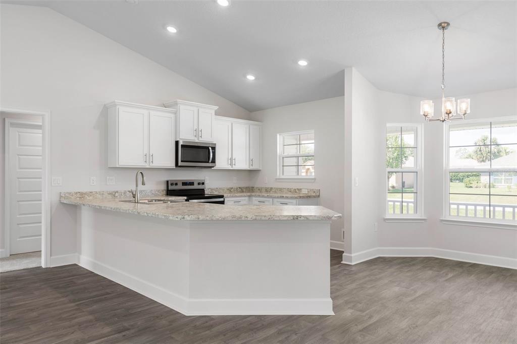 A kitchen with white cabinets, granite countertops, and a breakfast bar overlooking a dining area — 2 ULMACEAL PATH, PALM COAST, FL