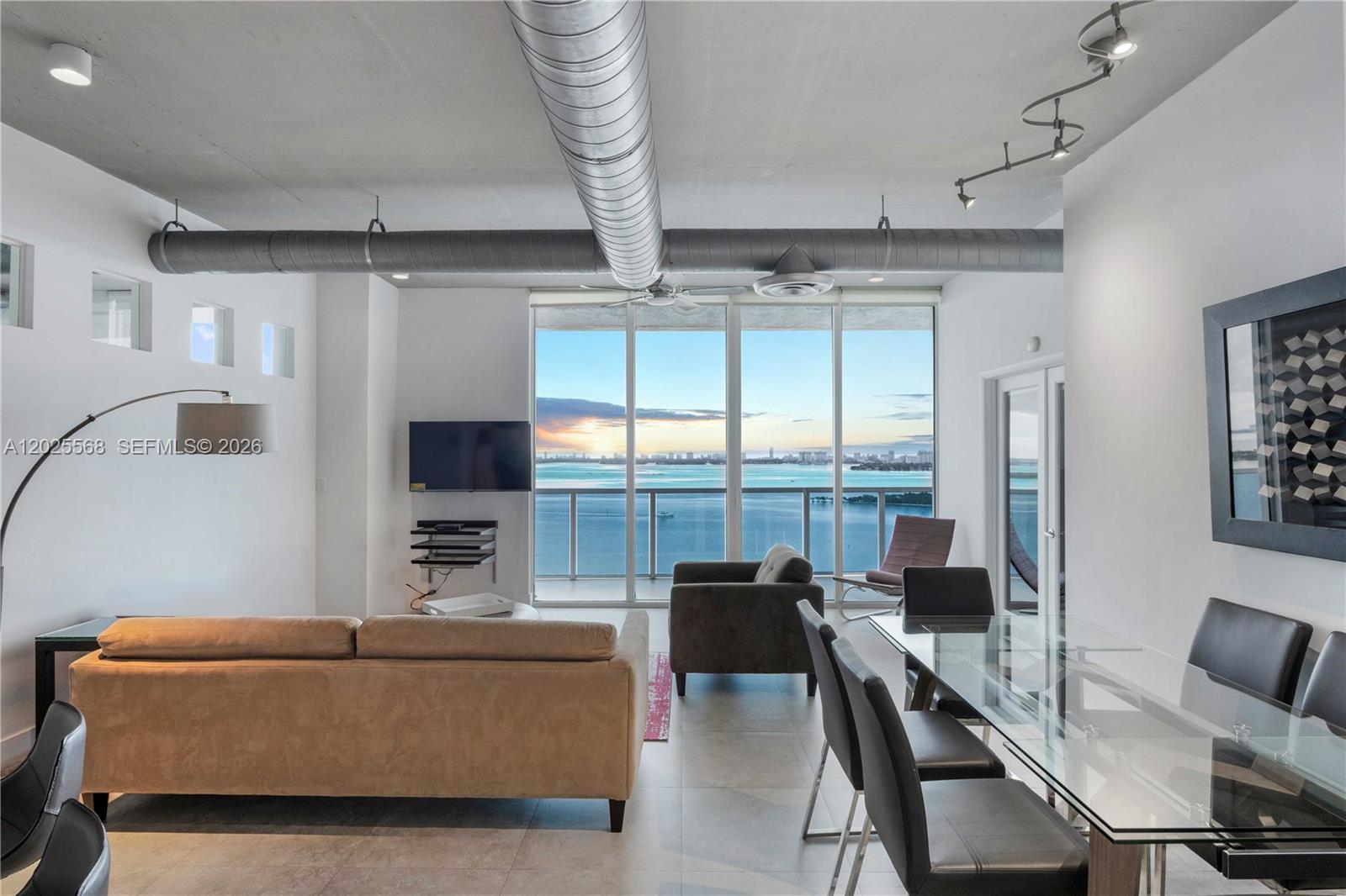 A living and dining area features industrial ductwork, floor-to-ceiling windows, and a waterfront view — 700 NE 25th St # 1902, Miami FL 33137, MIAMI, FL
