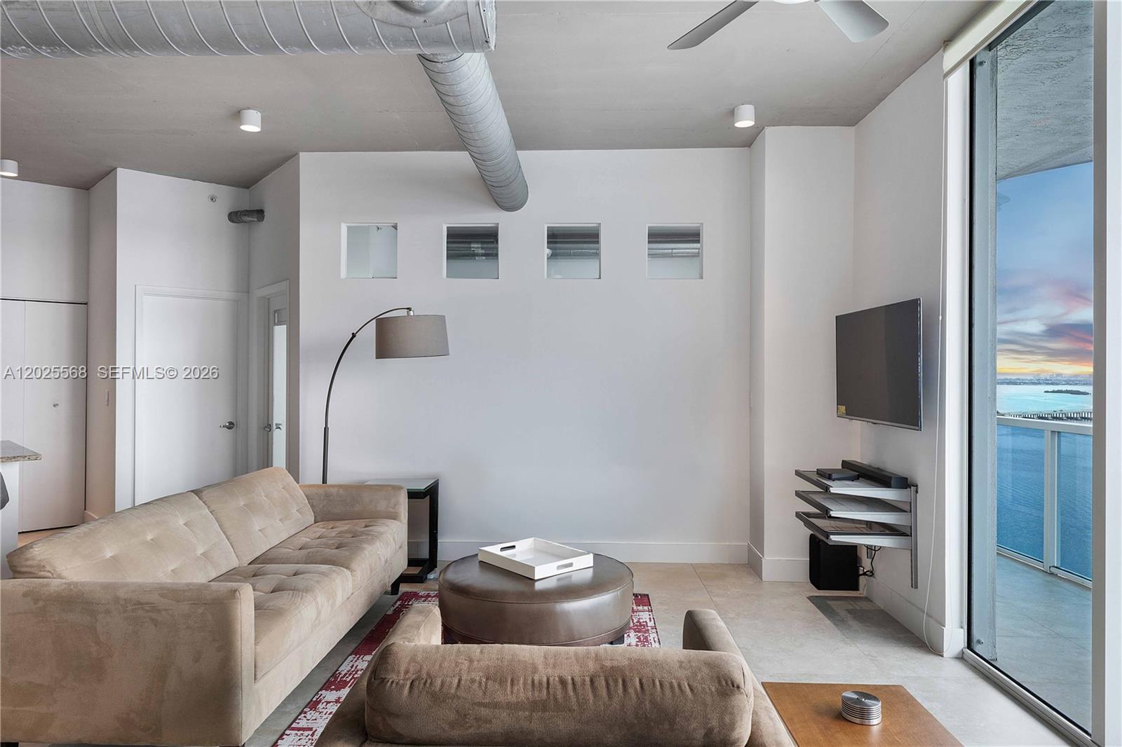 A living room features a beige sofa, a round ottoman, and a balcony with water views — 700 NE 25th St # 1902, Miami FL 33137, MIAMI, FL