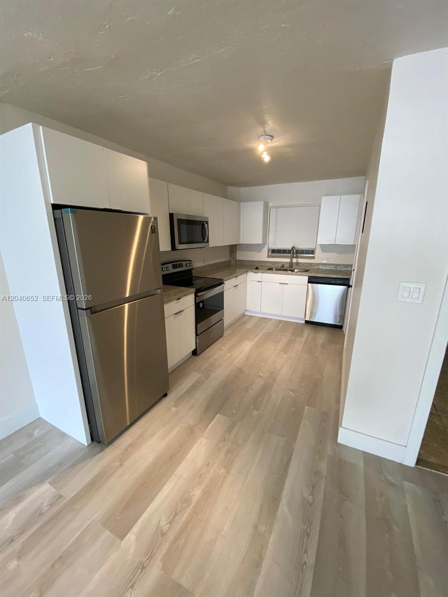 A kitchen features white cabinets, stainless steel appliances, and light wood-look flooring — 1939 Jefferson St # 102, Hollywood FL 33020, HOLLYWOOD, FL