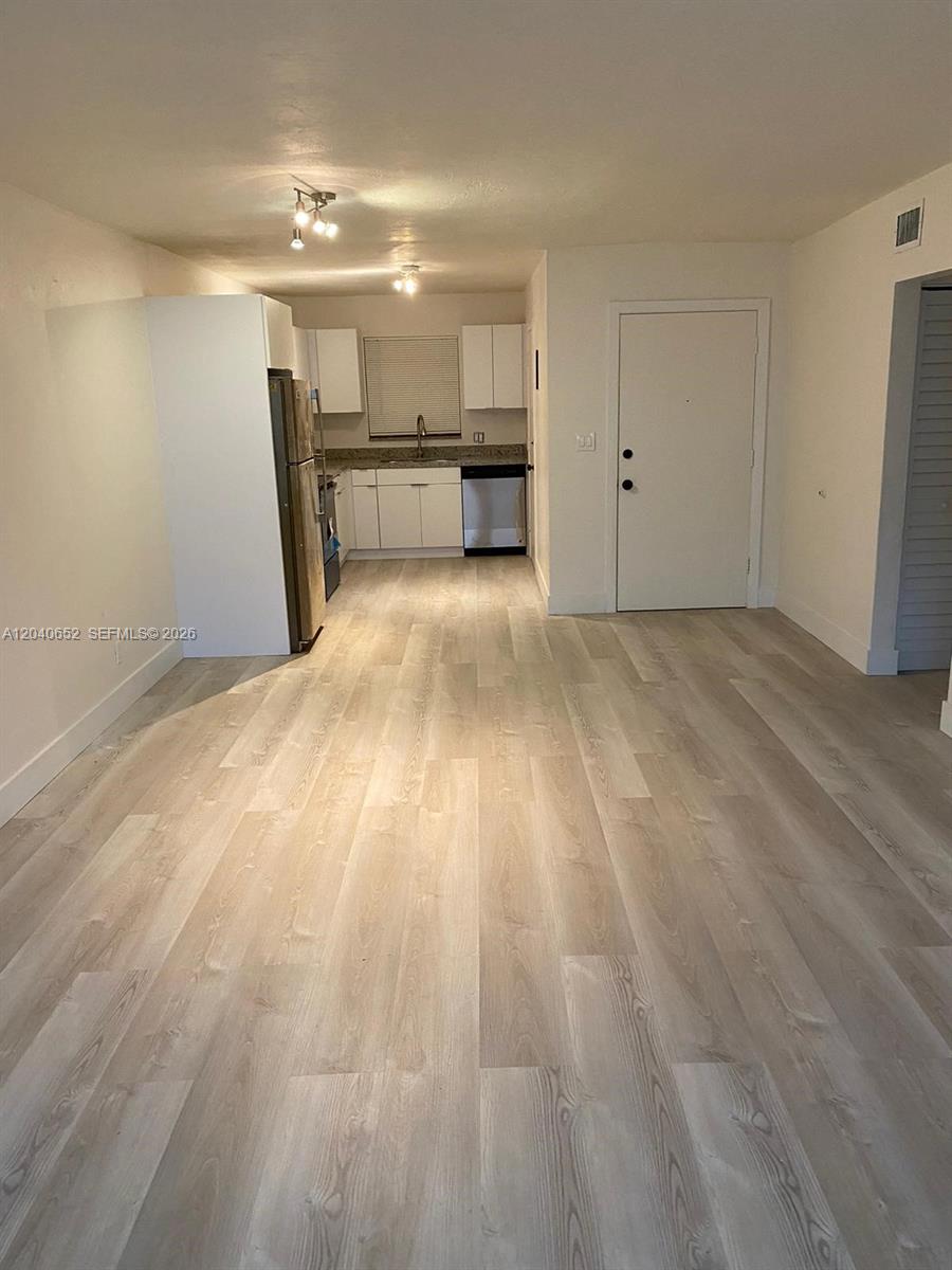 An open-concept living area features light wood-look flooring and a kitchen with white cabinets — 1939 Jefferson St # 102, Hollywood FL 33020, HOLLYWOOD, FL