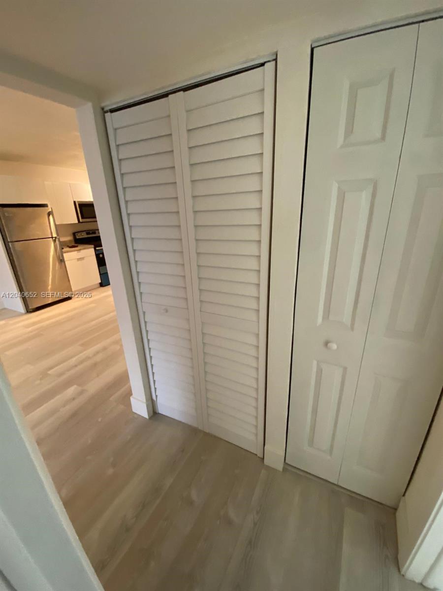 A hallway features light wood-look flooring, a louvered closet door, and a view into a kitchen — 1939 Jefferson St # 102, Hollywood FL 33020, HOLLYWOOD, FL