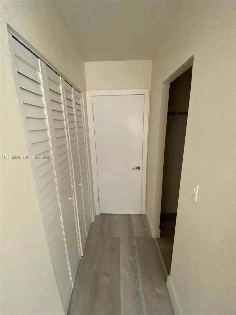 A hallway features light wood-look flooring, white louvered closet doors, and a closed interior door — 1939 Jefferson St # 102, Hollywood FL 33020, HOLLYWOOD, FL