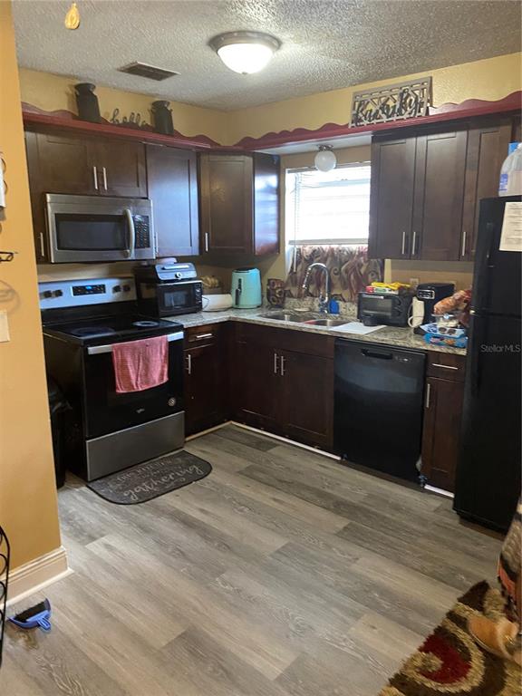 A kitchen features dark wood cabinets, stainless steel appliances, and wood-look flooring — 5520 20TH STREET, ZEPHYRHILLS, FL