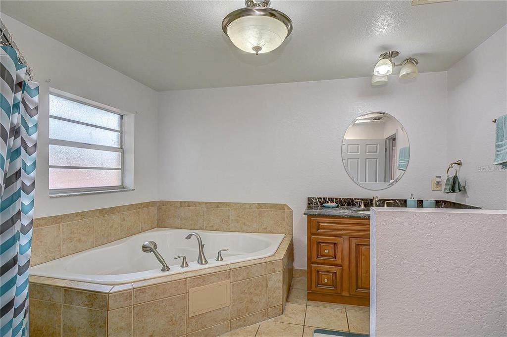 A bathroom features a tiled corner soaking tub, a wooden vanity, and a round mirror — 5520 20TH STREET, ZEPHYRHILLS, FL