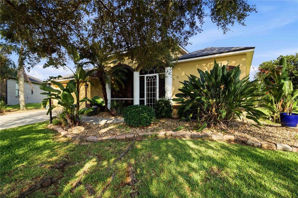A yellow house with a screened front porch and large tropical plants in the yard — 2915 126TH TERRACE E, PARRISH, FL