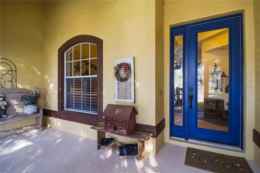 A covered porch features a blue front door, a window, and rustic wooden furniture — 2915 126TH TERRACE E, PARRISH, FL