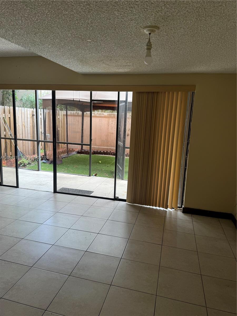 A room with light-colored floor tiles, a popcorn ceiling, and a sliding glass door to a patio — 8024 NW 27th Ct, Sunrise FL 33322, SUNRISE, FL