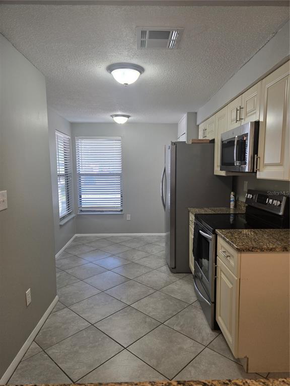 A kitchen features light-colored cabinets, granite countertops, stainless steel appliances, and gray tile flooring — 787 ARTHURS COURT, TARPON SPRINGS, FL