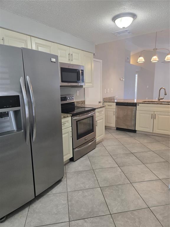 A kitchen features stainless steel appliances, cream-colored cabinetry, granite countertops, and light-colored tile flooring — 787 ARTHURS COURT, TARPON SPRINGS, FL