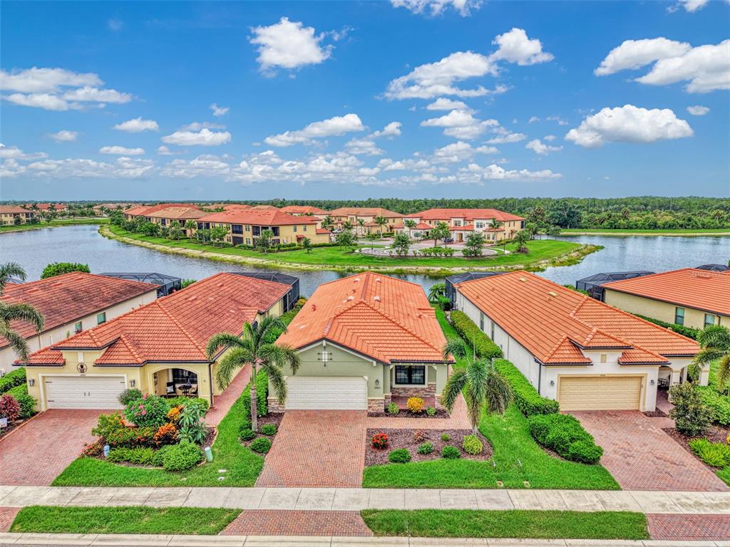 An aerial view shows three suburban houses with terracotta tile roofs facing a lake — 10065 COZY GROVE DRIVE, VENICE, FL