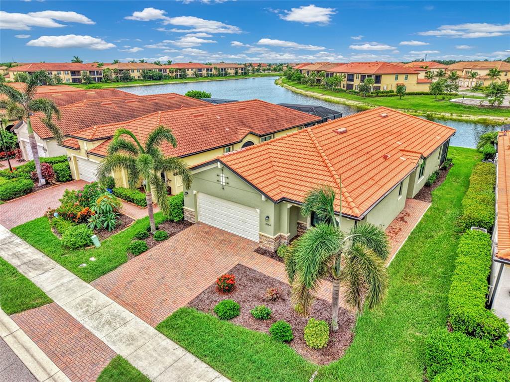 An aerial view of a suburban house with a tile roof, brick driveway, and palm trees — 10065 COZY GROVE DRIVE, VENICE, FL