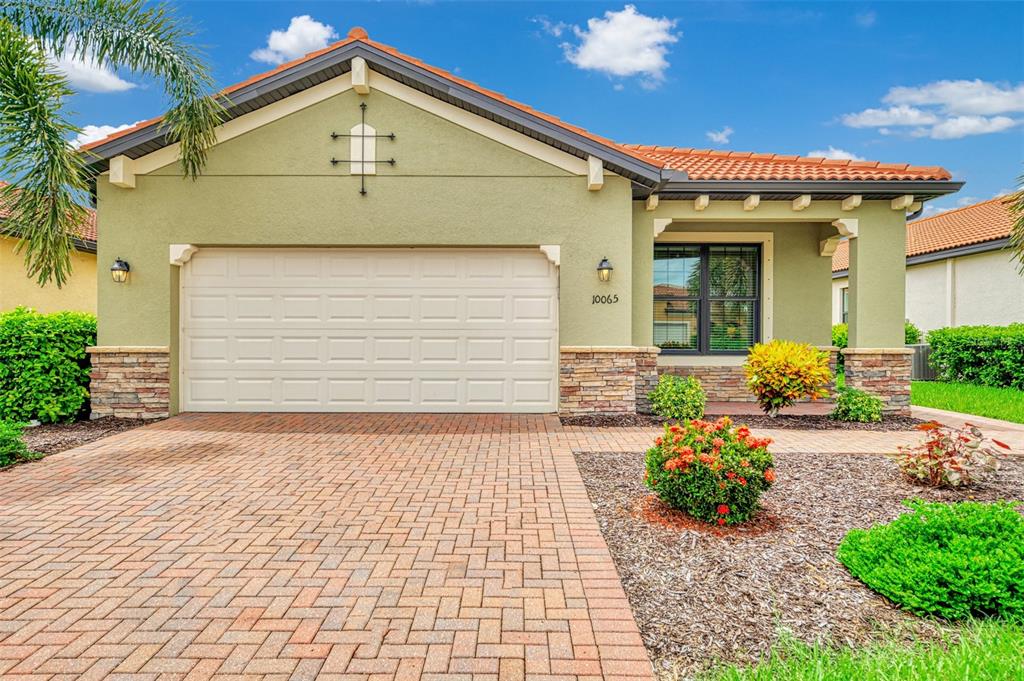 A single-story house with a green stucco exterior, a tile roof, and a brick paver driveway — 10065 COZY GROVE DRIVE, VENICE, FL