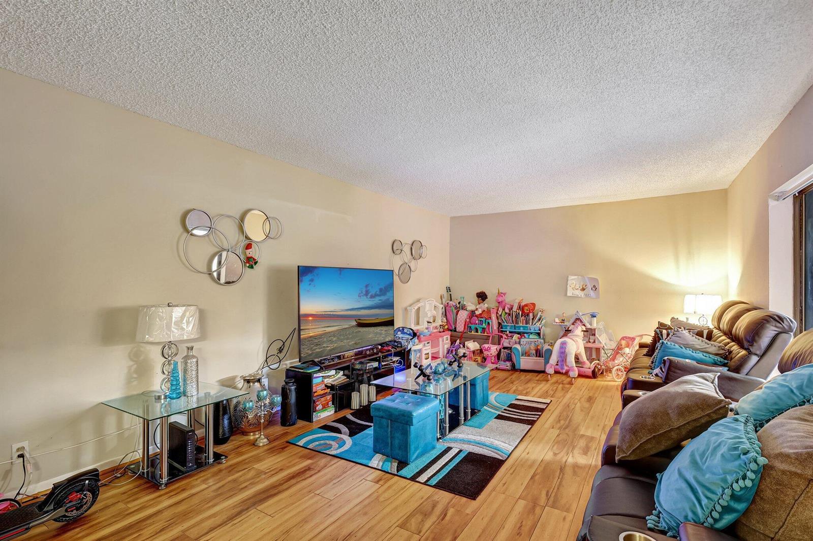 A living room features wood-look flooring, a large television, a blue area rug, and seating — 5852 SE Riverboat Drive # 321, Stuart FL 34997, STUART, FL