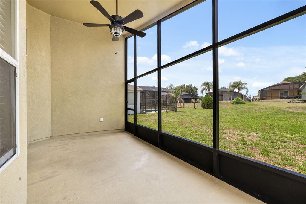 A covered screened-in patio with a ceiling fan overlooks a grassy backyard and neighboring houses — 3108 MERLOT WAY, CLERMONT, FL