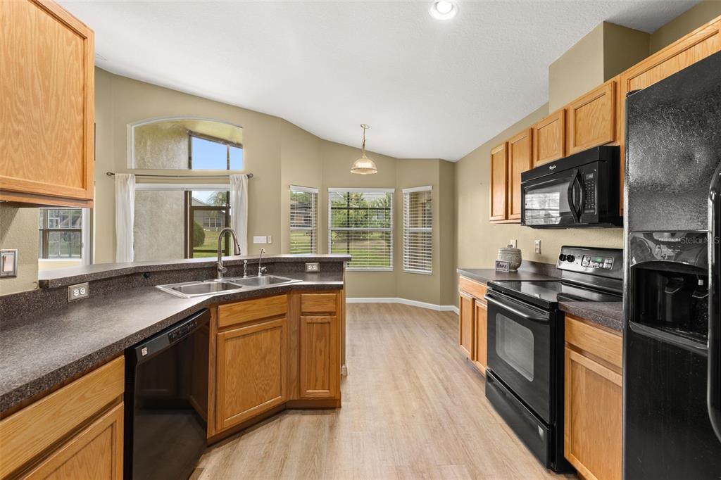 A kitchen with oak cabinets, dark countertops, black appliances, and a breakfast nook with windows — 3108 MERLOT WAY, CLERMONT, FL