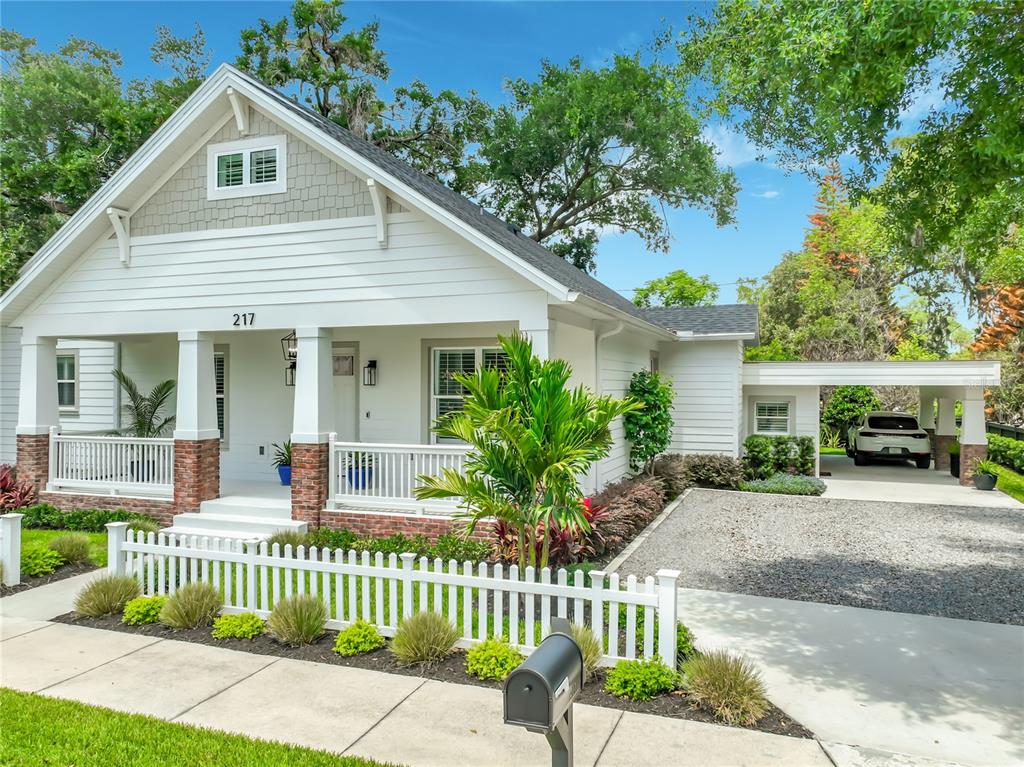 A white bungalow with a front porch, brick accents, and a gravel driveway with a carport — 217 W BAY STREET, WINTER GARDEN, FL