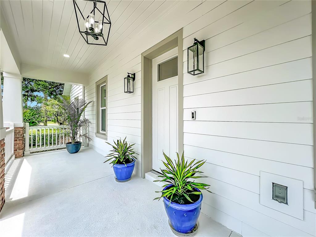 A covered front porch features white horizontal siding, a white door, and blue potted plants — 217 W BAY STREET, WINTER GARDEN, FL