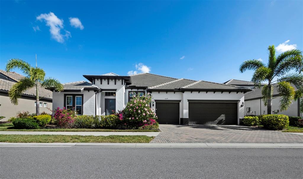 A single-story house with a white stucco exterior, dark trim, and a paved driveway — 6129 LUNGO LAGO DRIVE, SARASOTA, FL