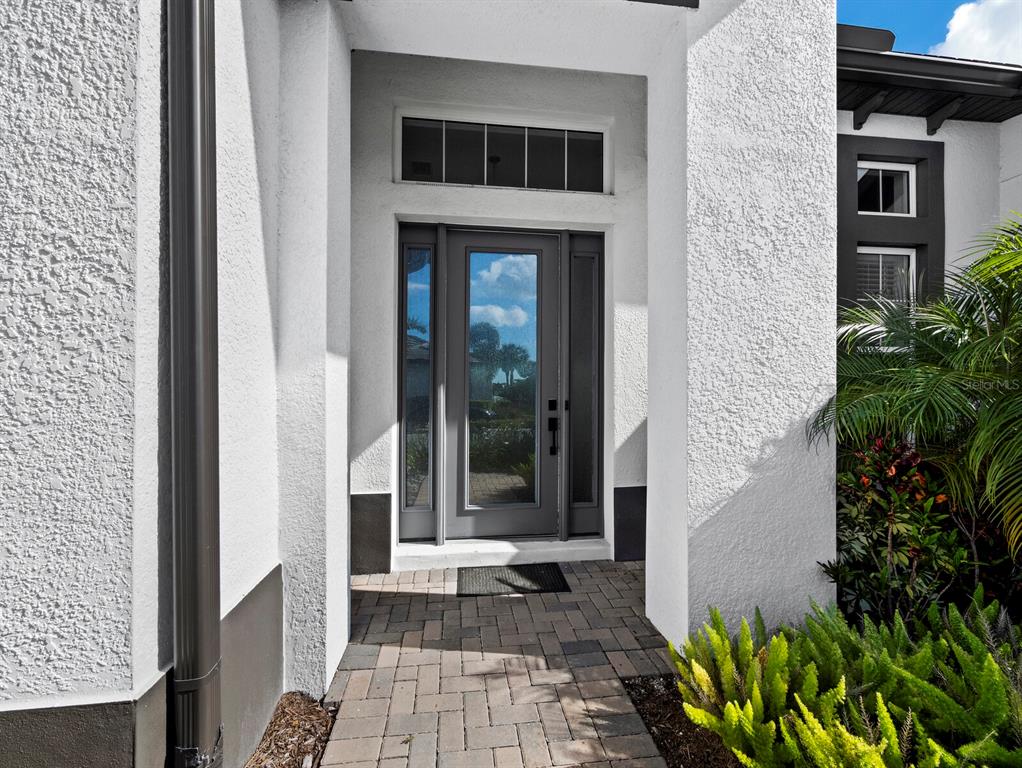 A front entryway features a glass-paneled door, a transom window, and a paved walkway — 6129 LUNGO LAGO DRIVE, SARASOTA, FL