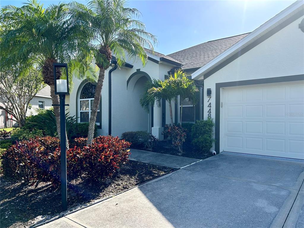 A single-story house exterior features a white garage door, a palm tree, and landscaping — 7448 39TH COURT E, SARASOTA, FL