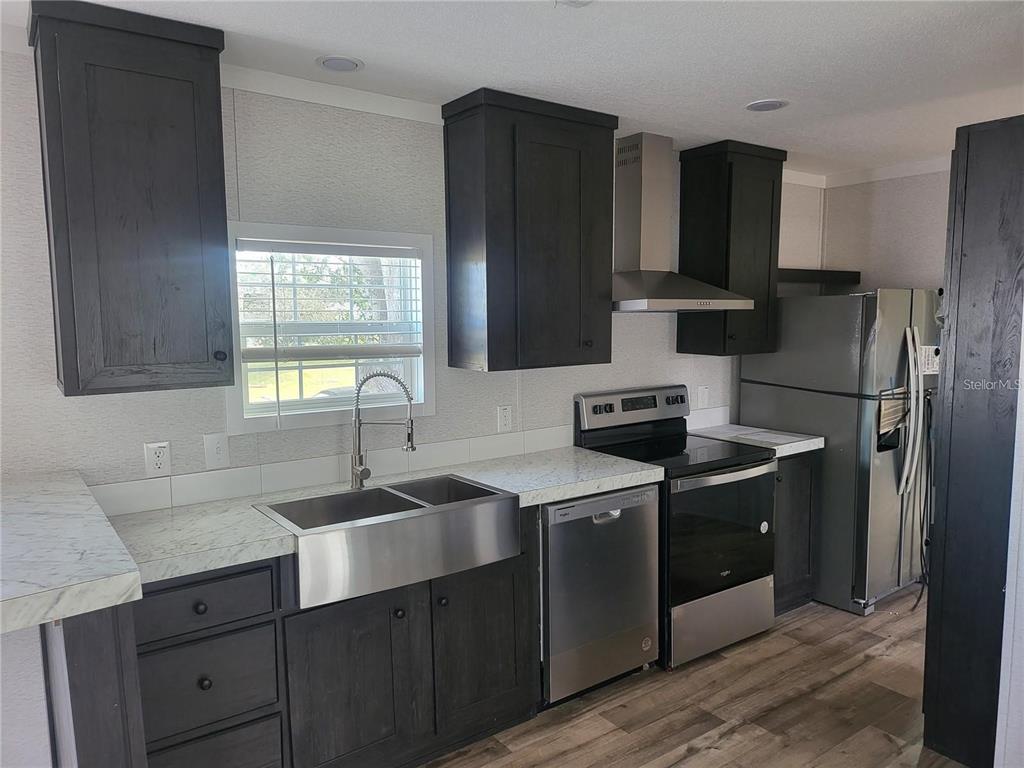 A kitchen features dark wood cabinets, stainless steel appliances, a farmhouse sink, and marble countertops — 4772 DUNCAN ROAD, PUNTA GORDA, FL