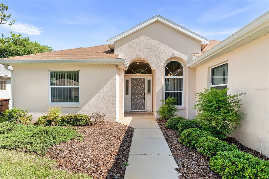 A beige, single-story house with a tan shingled roof, arched entryway, and landscaped front yard — 11295 SW 73RD CIRCLE, OCALA, FL