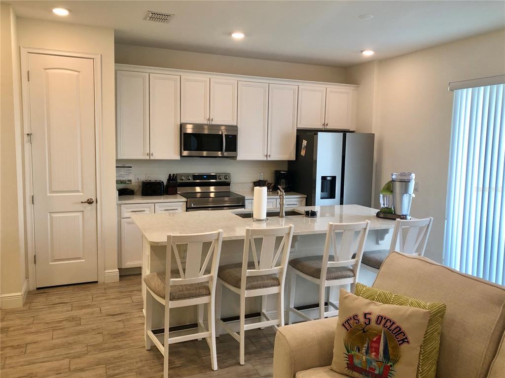 A kitchen features white cabinets, stainless steel appliances, a quartz island, and light wood flooring — 2972 ON THE ROCKS POINT, KISSIMMEE, FL