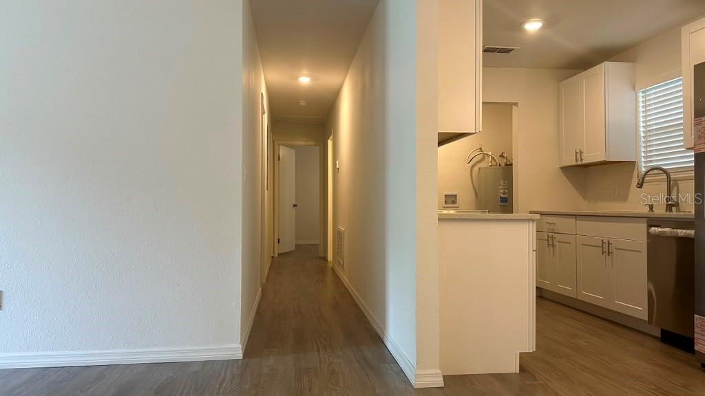 A hallway leads to a bedroom past a kitchen with white cabinets and wood flooring — 5920 NW 65TH STREET, OCALA, FL