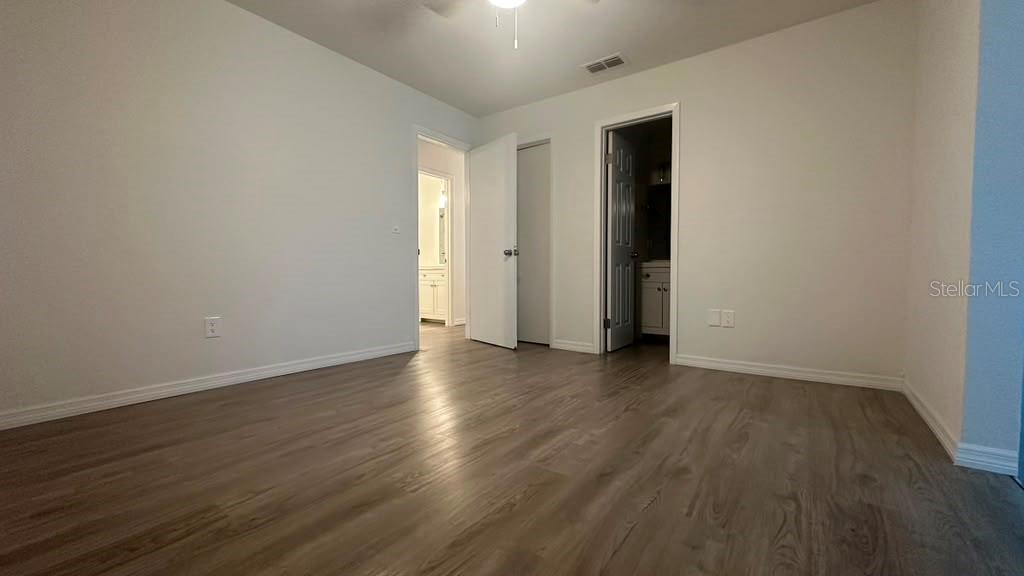 A bedroom with light-colored walls, wood-look flooring, a ceiling fan, and two open doorways — 5920 NW 65TH STREET, OCALA, FL