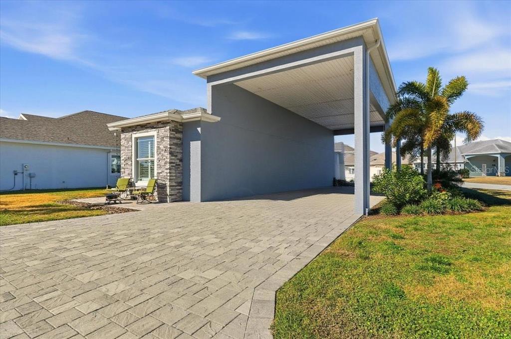 A paved driveway leads to a covered carport attached to a house with stone siding — 303 NOLANE LANE, POLK CITY, FL