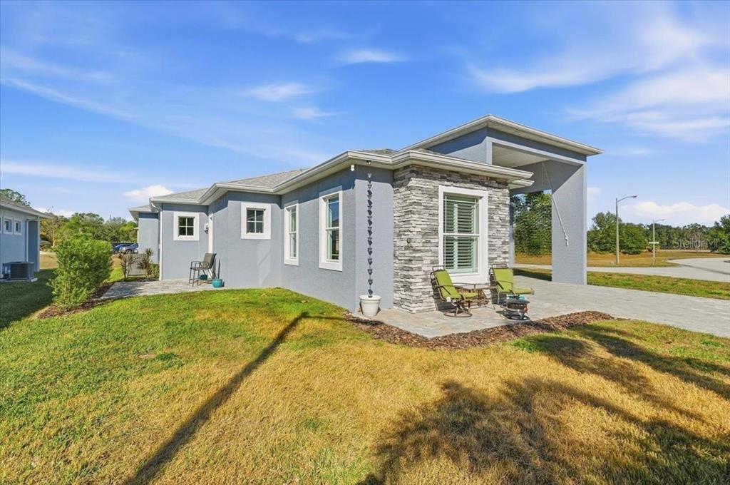 A gray house with a stone facade, a covered patio, and a grassy yard — 303 NOLANE LANE, POLK CITY, FL