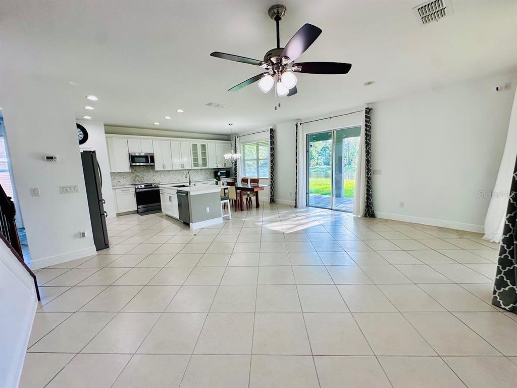 An open-concept kitchen and living area features tile flooring, white cabinetry, and a ceiling fan — 10726 CABBAGE TREE LOOP, ORLANDO, FL