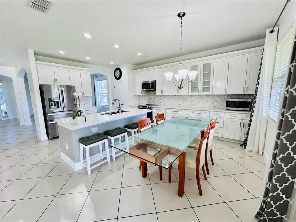 A kitchen with white cabinetry, a central island, and a glass-topped dining table — 10726 CABBAGE TREE LOOP, ORLANDO, FL