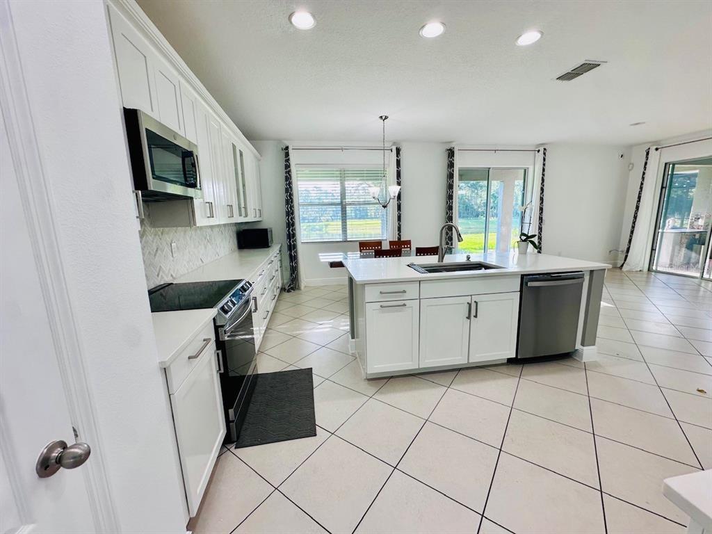 A bright kitchen features white cabinets, stainless steel appliances, a center island, and tile flooring — 10726 CABBAGE TREE LOOP, ORLANDO, FL