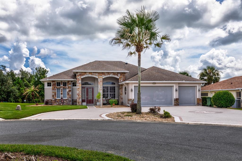 A single-story house with a stone facade, a three-car garage, and a palm tree — 27028 OLD ENGLISH COURT, LEESBURG, FL