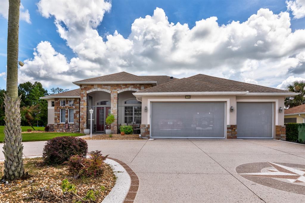 A single-story house with a stone facade, a three-car garage, and a concrete driveway — 27028 OLD ENGLISH COURT, LEESBURG, FL
