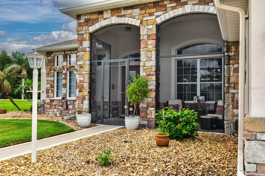 A stone-faced house exterior features a screened-in porch, a gravel yard, and a white lamp — 27028 OLD ENGLISH COURT, LEESBURG, FL