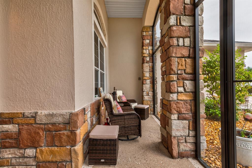 A covered patio features stone pillars, wicker chairs, and a screened-in view of the yard — 27028 OLD ENGLISH COURT, LEESBURG, FL