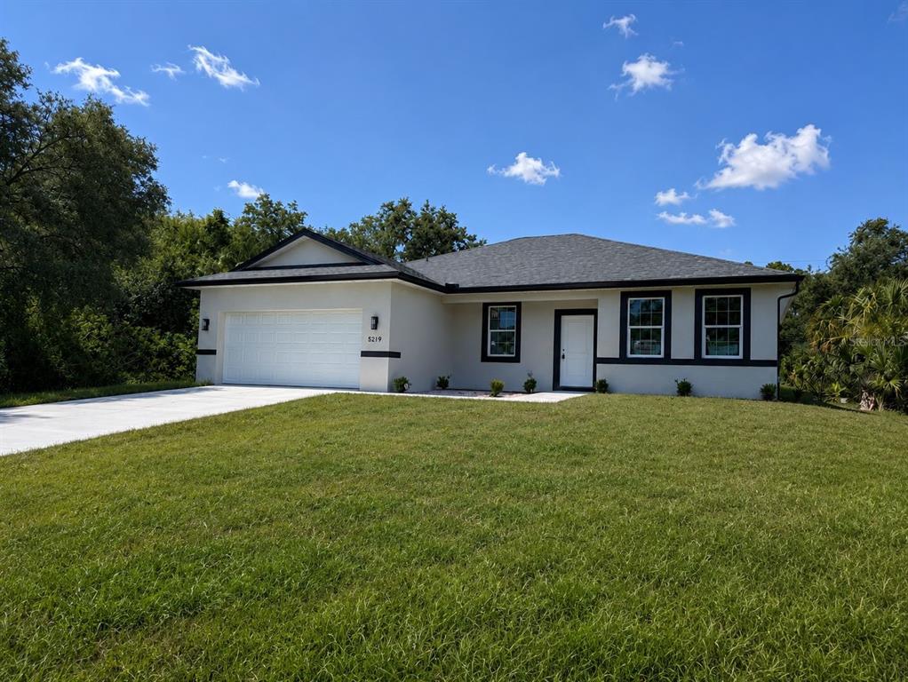 A single-story house with a white stucco exterior, dark trim, and a two-car garage — 5219 SYLVANIA AVENUE, NORTH PORT, FL