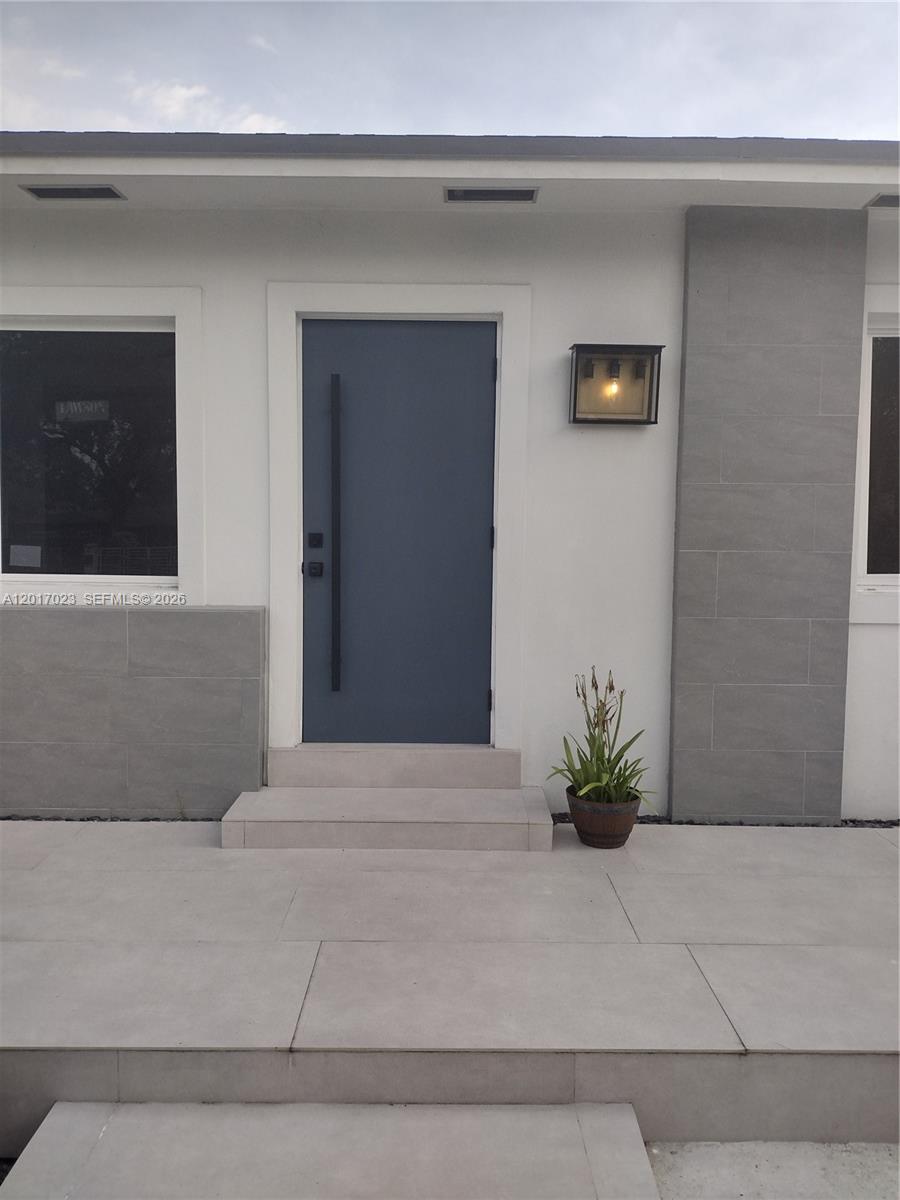 A modern home exterior features a blue front door, gray tile accents, and concrete steps — 300 S Biscayne River Dr, Miami FL 33169, MIAMI, FL