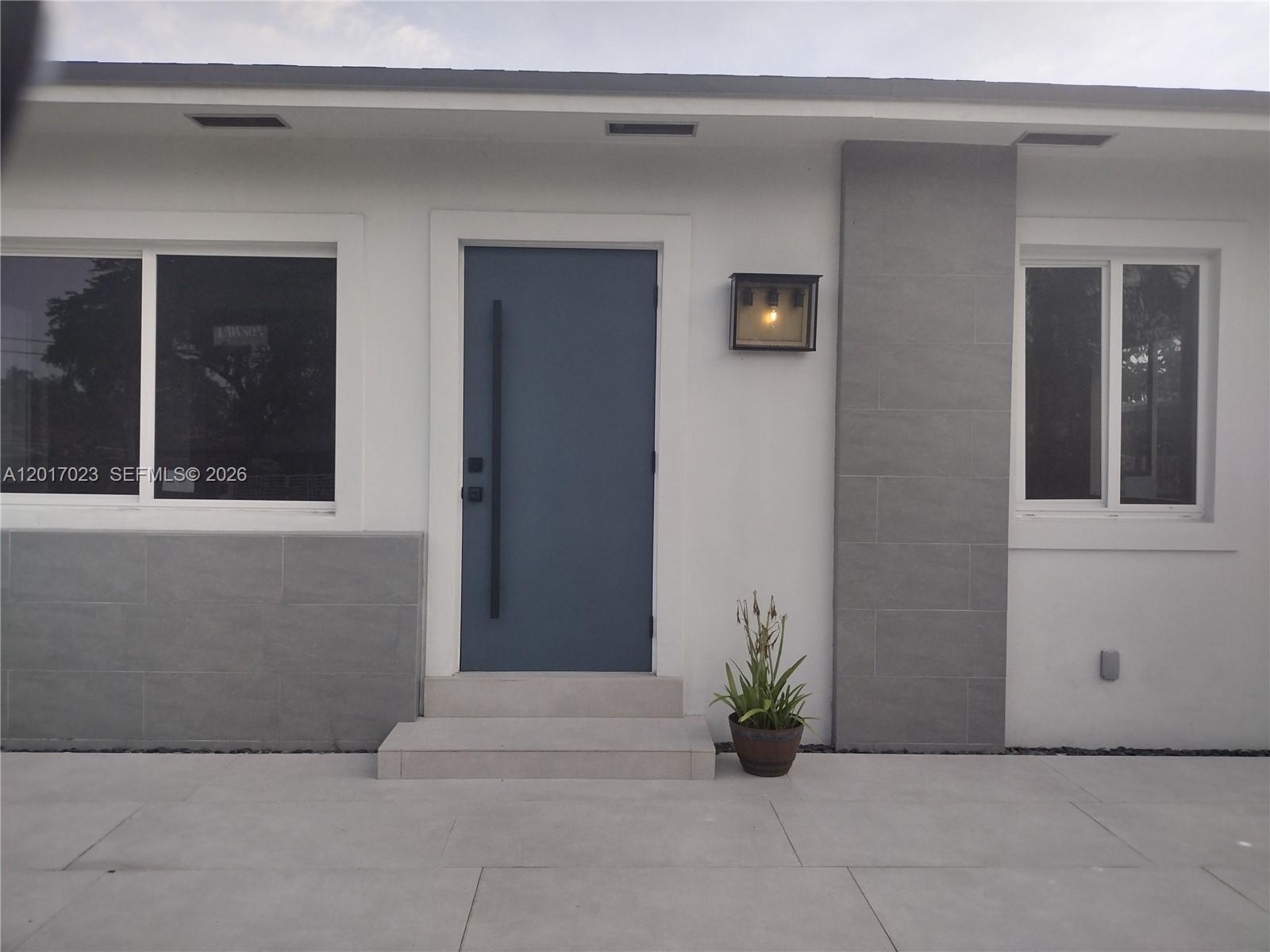 A modern home exterior features a blue door, gray tile accents, and a concrete patio — 300 S Biscayne River Dr, Miami FL 33169, MIAMI, FL