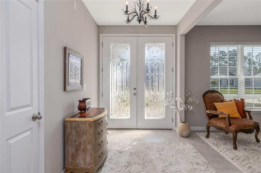 A bright entryway features double glass-paneled doors, a chandelier, a wooden chest, and an armchair — 139 WOOD STORK LANE, PALM COAST, FL