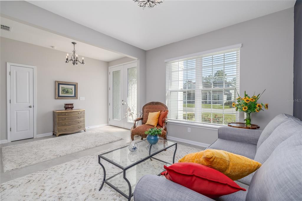 A living room features a glass coffee table, gray sofa, patterned armchair, and front entryway — 139 WOOD STORK LANE, PALM COAST, FL