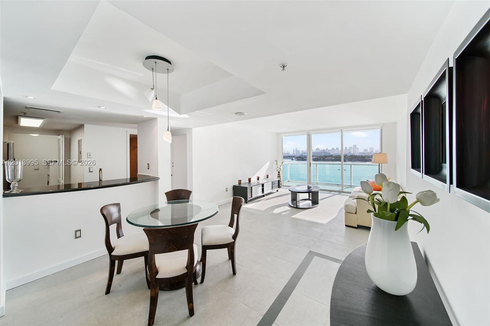 A bright living and dining area features a glass table, modern furniture, and balcony views — 650 West Ave # 805, Miami Beach FL 33139, MIAMI BEACH, FL
