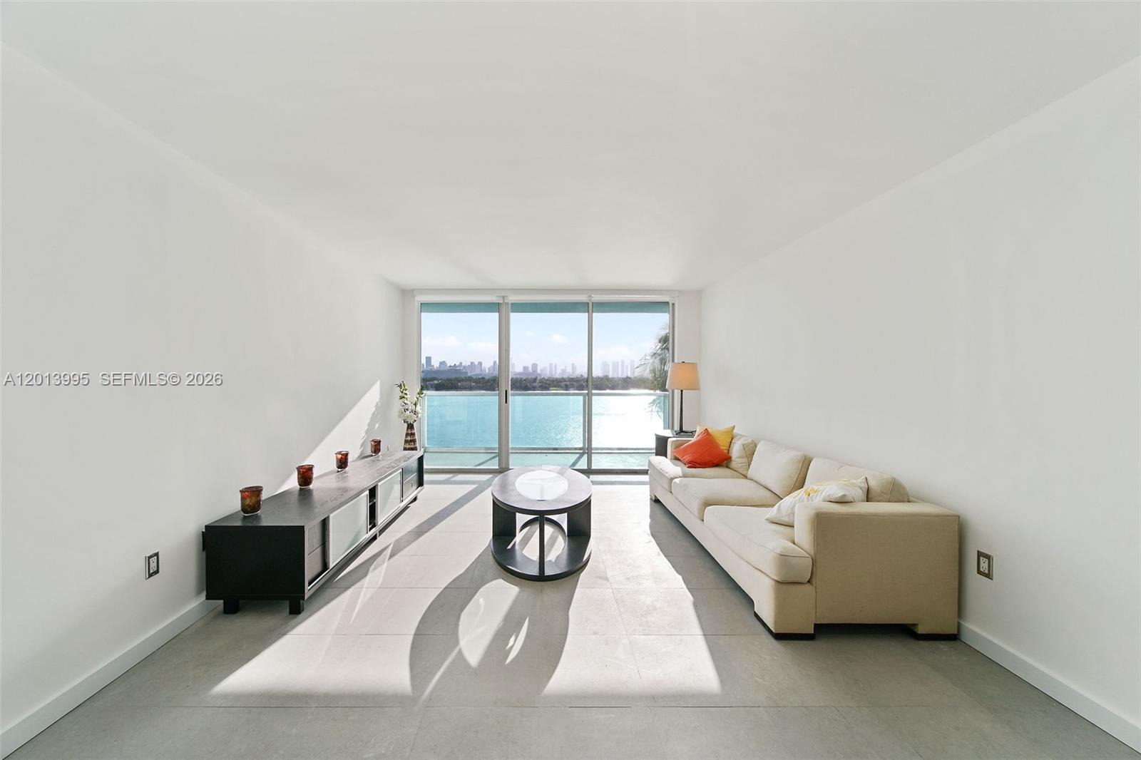 A living room features a beige sofa, a black media console, and a waterfront view — 650 West Ave # 805, Miami Beach FL 33139, MIAMI BEACH, FL