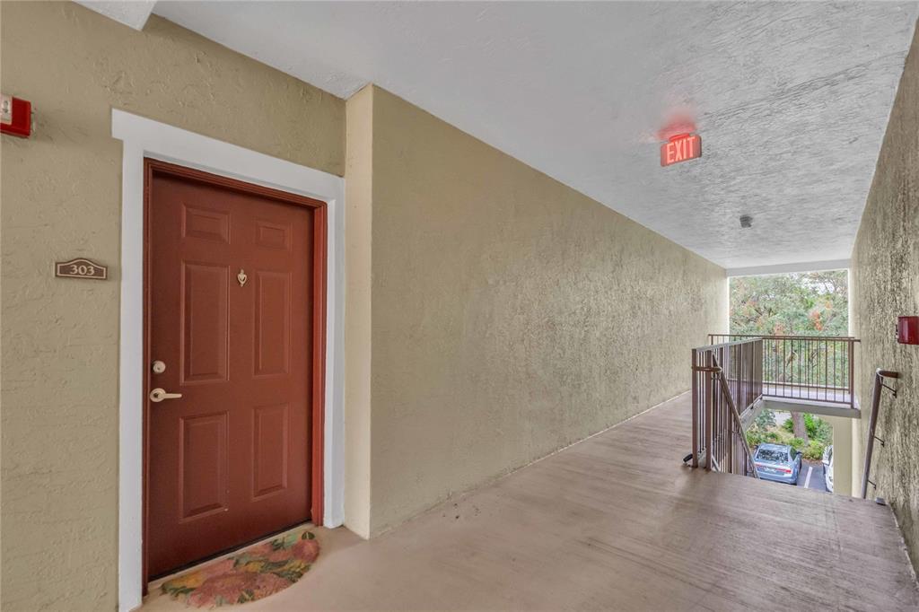 An exterior apartment hallway features a brown door numbered 303 and a metal stairwell — 4763 TRAVINI CIRCLE UNIT 3-303, SARASOTA, FL