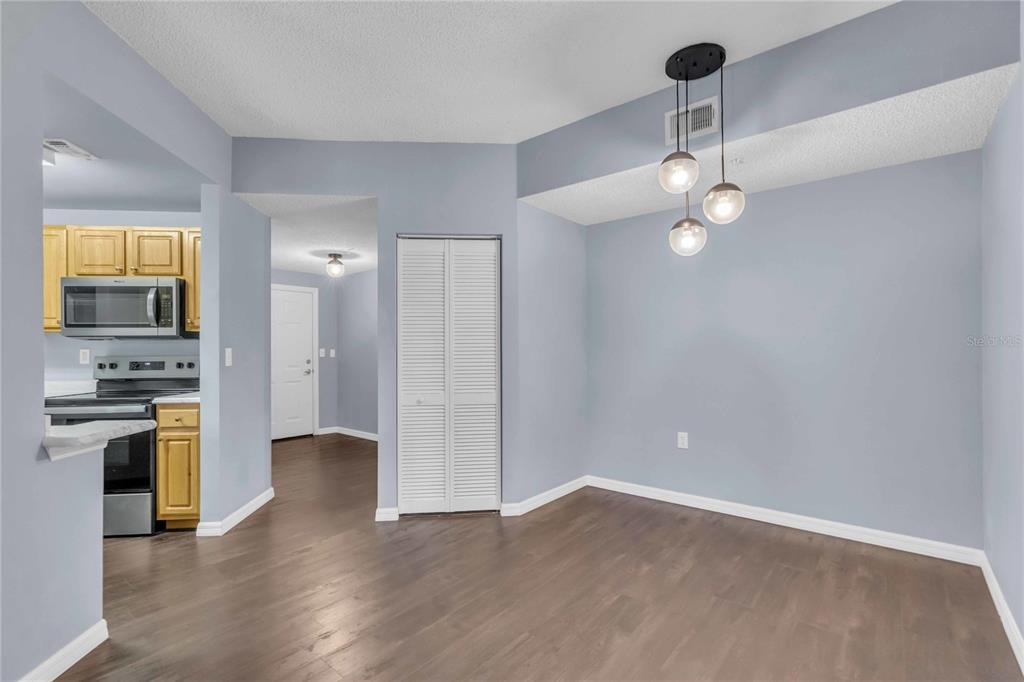 A dining area with light blue walls, wood-look flooring, and a modern three-globe pendant light — 4763 TRAVINI CIRCLE UNIT 3-303, SARASOTA, FL